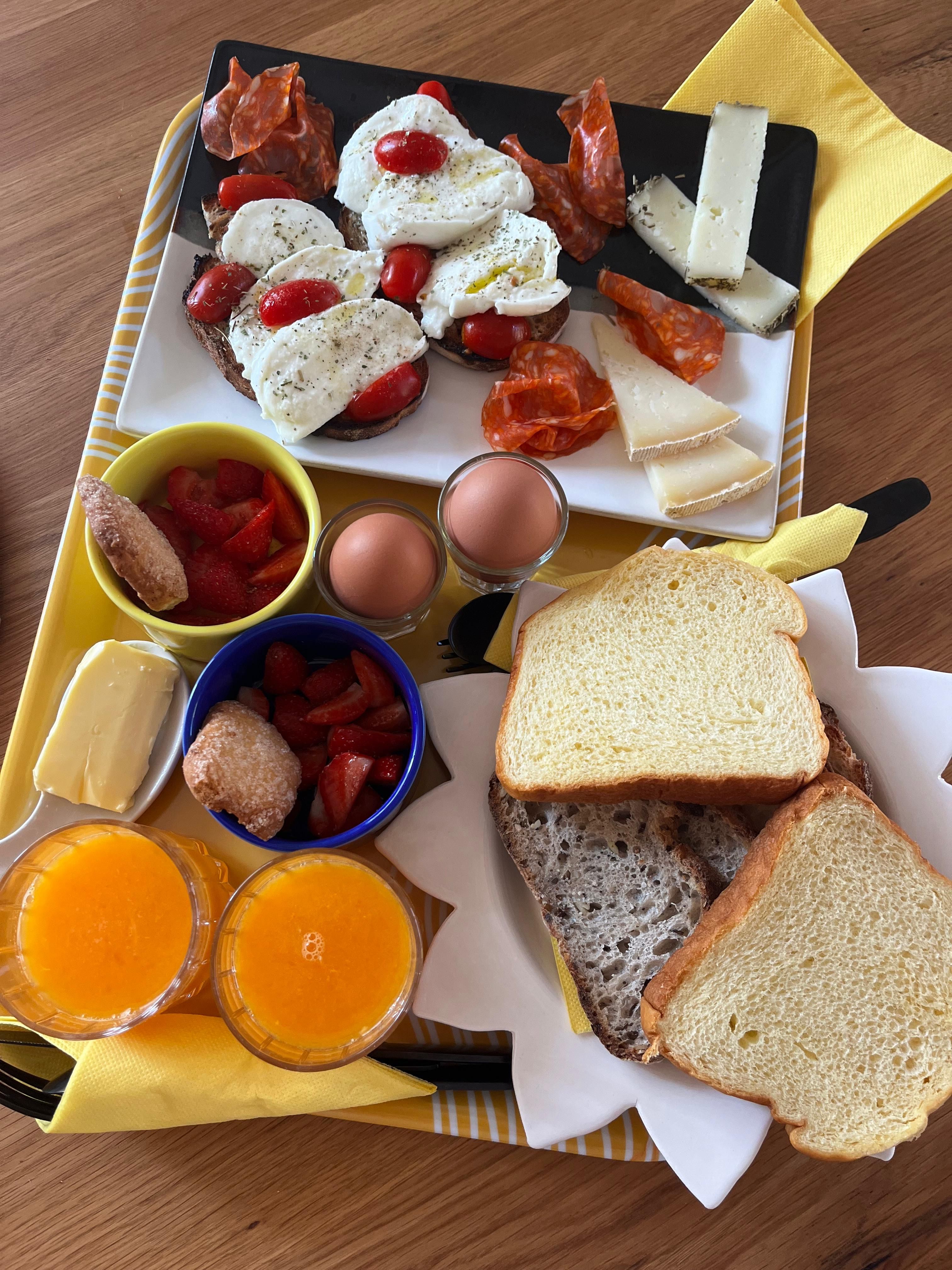 Breakfast tray: tomato and mozzarella toasts, charcuterie, cheeses, eggs, strawberries, doughnuts, brioche and fresh orange juice