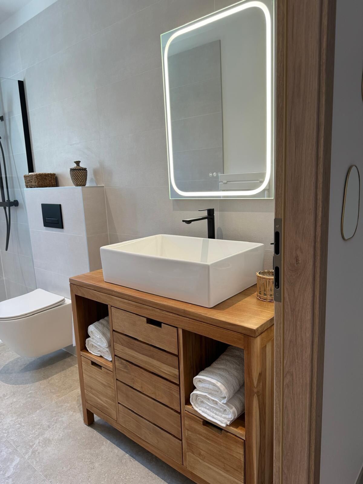 White basin on a wooden vanity unit and illuminated mirror in the shower room